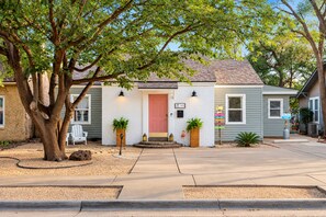A two-story house with a red door, white brick walls, and a front yard with a tree and two potted plants. - The Island – Two Homes, One Paradise! (Lubbock)