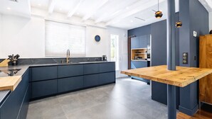 Une cuisine moderne dotée d’un îlot central, de meubles de rangement aux couleurs sombres et d’une table à manger en bois.