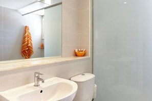 Casa de banho com lavatório branco, sanita e espelho.