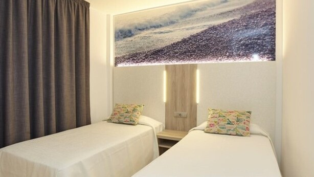 Ett hotellrum med två separata sängar, ett stort konstverk som föreställer en strandscen och som hänger på väggen, samt en gardin på vänster sida.