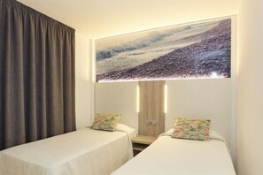 Una habitación de hotel con dos camas individuales, una obra de arte grande en la pared que muestra una escena de playa y una cortina a la izquierda.