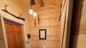 Un intérieur en bois, avec une porte en bois, un banc, une petite table sur laquelle se trouve une boîte de mouchoirs, et un menu encadré accroché au mur.
