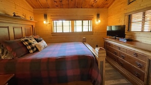 Une pièce chaleureuse, aménagée dans un chalet en bois, avec un lit, une commode et un téléviseur.