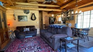 L’intérieur d’un chalet confortable, avec un plafond en bois, un grand canapé, une table à manger entourée de chaises et un coin cuisine.