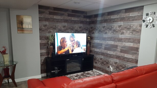 Un salon avec un canapé en cuir rouge, un téléviseur fixé à un mur en bois et une petite table ornée d’objets décoratifs.