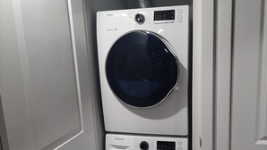 Une machine à laver et un sèche-linge superposés dans une pièce avec des portes blanches et un plancher en bois.