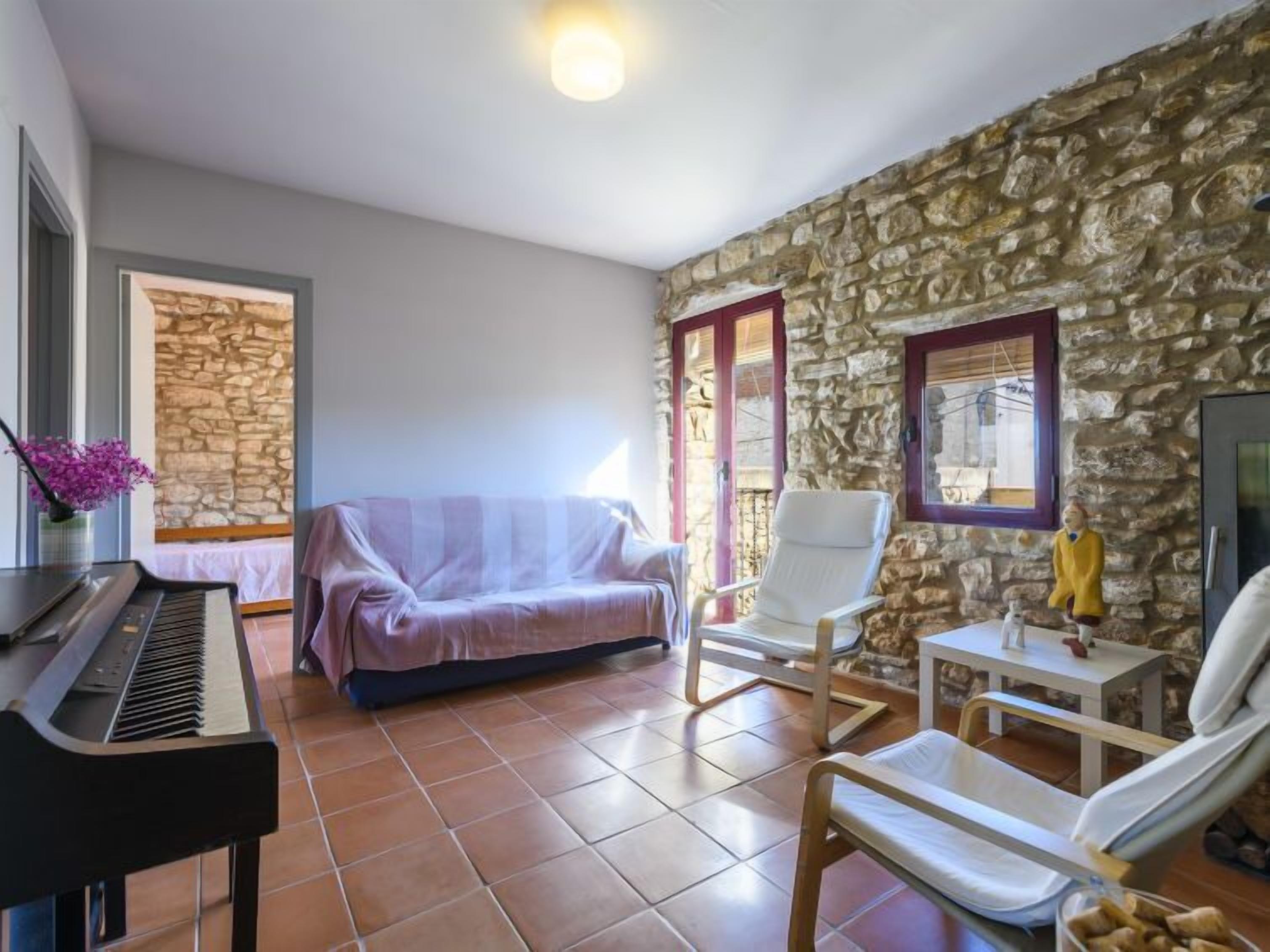 Habitació amb un piano, un sofà, una cadira i una paret de pedra.