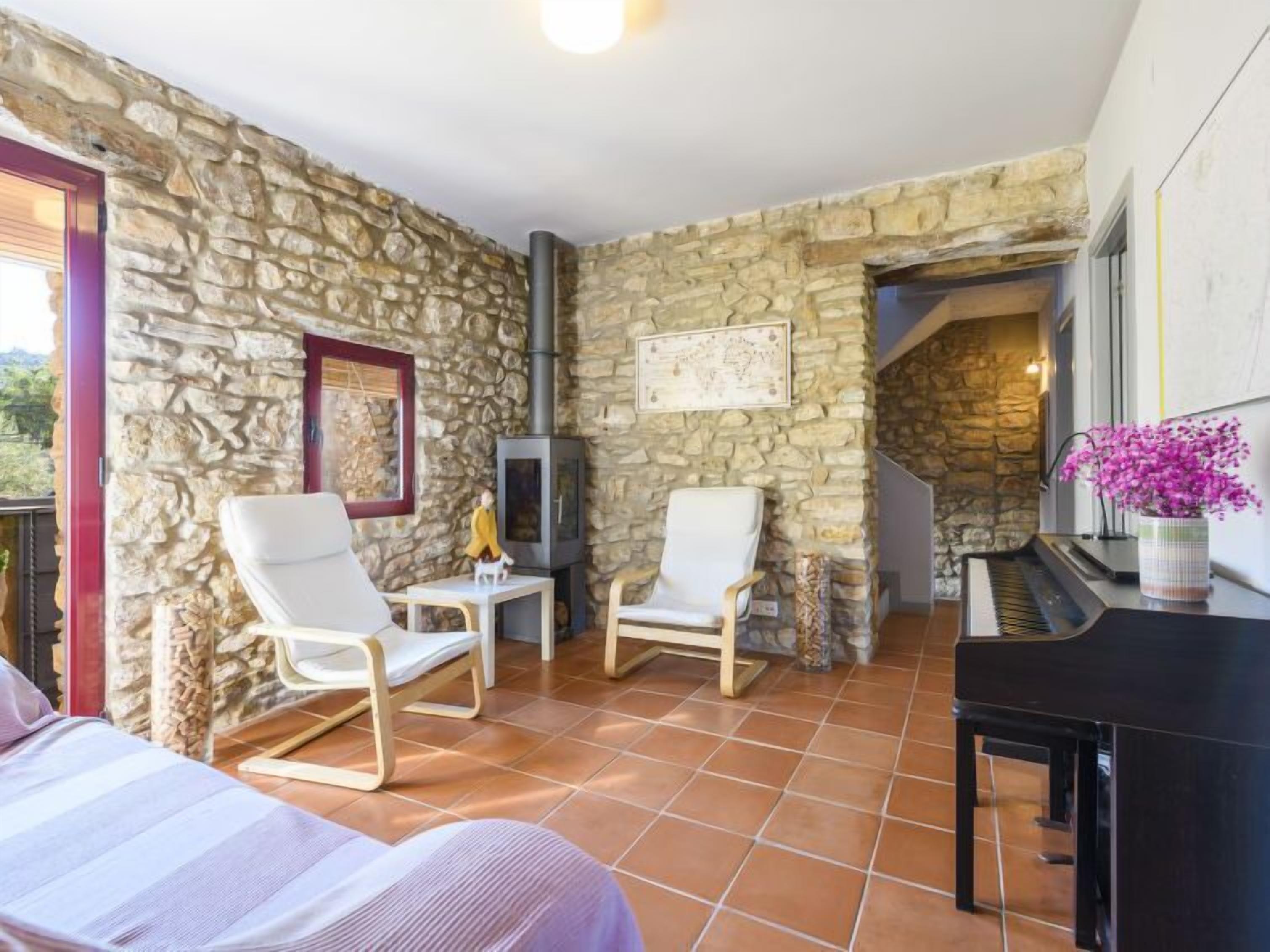 Une pièce chaleureuse avec des murs en pierre, une cheminée, un piano et deux fauteuils.