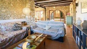 Una stanza rustica con parete in pietra, travi in legno, un divano, un letto e una libreria.