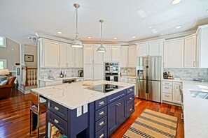 A modern kitchen with white cabinets, a central island with a marble countertop, stainless steel appliances, and pendant lighting.