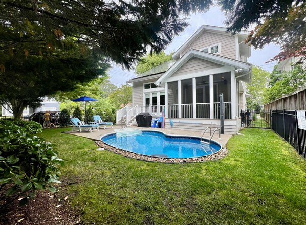 Un jardin avec une piscine, un patio couvert et un espace clos aménagé avec des chaises longues.
