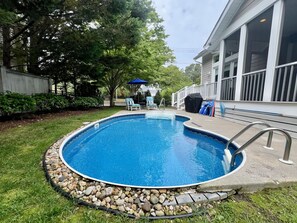 Une piscine située dans le jardin, bordée de pierres, et entourée de pelouse et d’arbres.