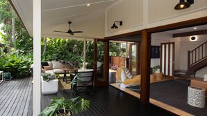 Ein großzügiger Wohnbereich mit Innen- und Außenbereich, einer Holzterrasse, einem Deckenventilator und einer Treppe, die in ein Obergeschoss führt.