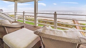 A covered outdoor seating area with wicker furniture and a view of the beach. - Oceanfront modern 4BR home with stunning views (Galveston)
