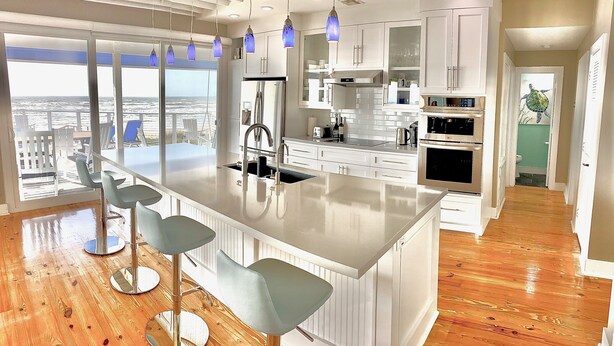A modern kitchen with a central island, bar stools, and a view of the city. - Oceanfront modern 4BR home with stunning views (Galveston)
