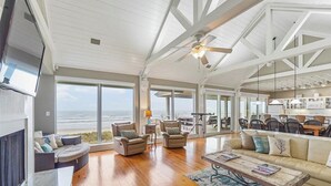 A spacious living room with a large window overlooking the ocean, wooden flooring, and a ceiling fan. - Oceanfront modern 4BR home with stunning views (Galveston)