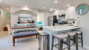 A modern kitchen with white cabinets, stainless steel appliances, and a large island with bar stools. There is a dining area with a bench and chairs, and a painting on the wall. - San Diego Beach Home/ Mission Beach,Steps to Ocean&Bay, 2 Car Garage, AC/Heating (San Diego)