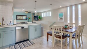 A modern kitchen with light blue cabinets, a dishwasher, and a dining area with a wooden table and chairs. - San Diego Beach Home/ Mission Beach,Steps to Ocean&Bay, 2 Car Garage, AC/Heating (San Diego)