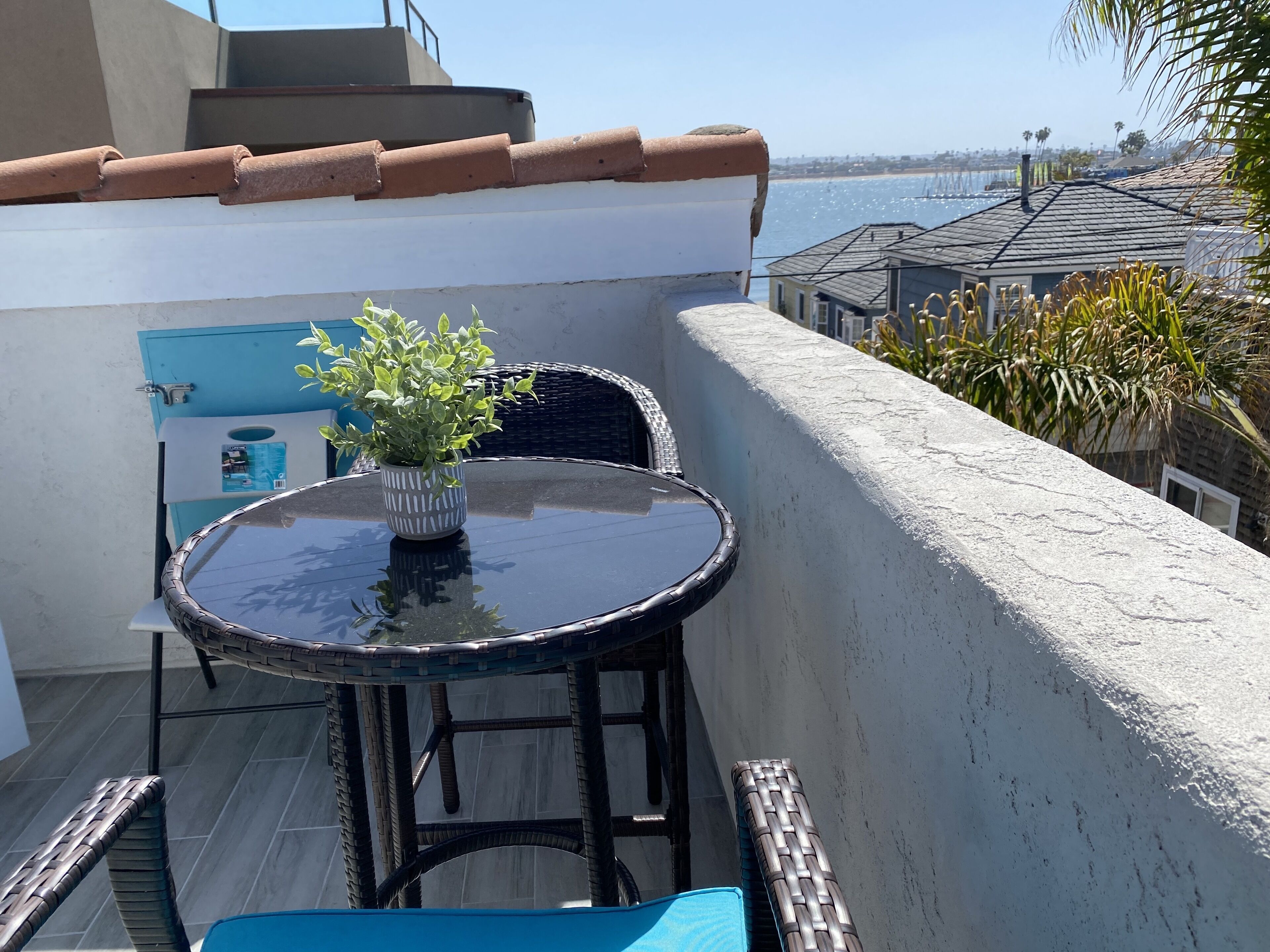Varanda com mesa, cadeiras, um vaso de planta e vista para o mar.