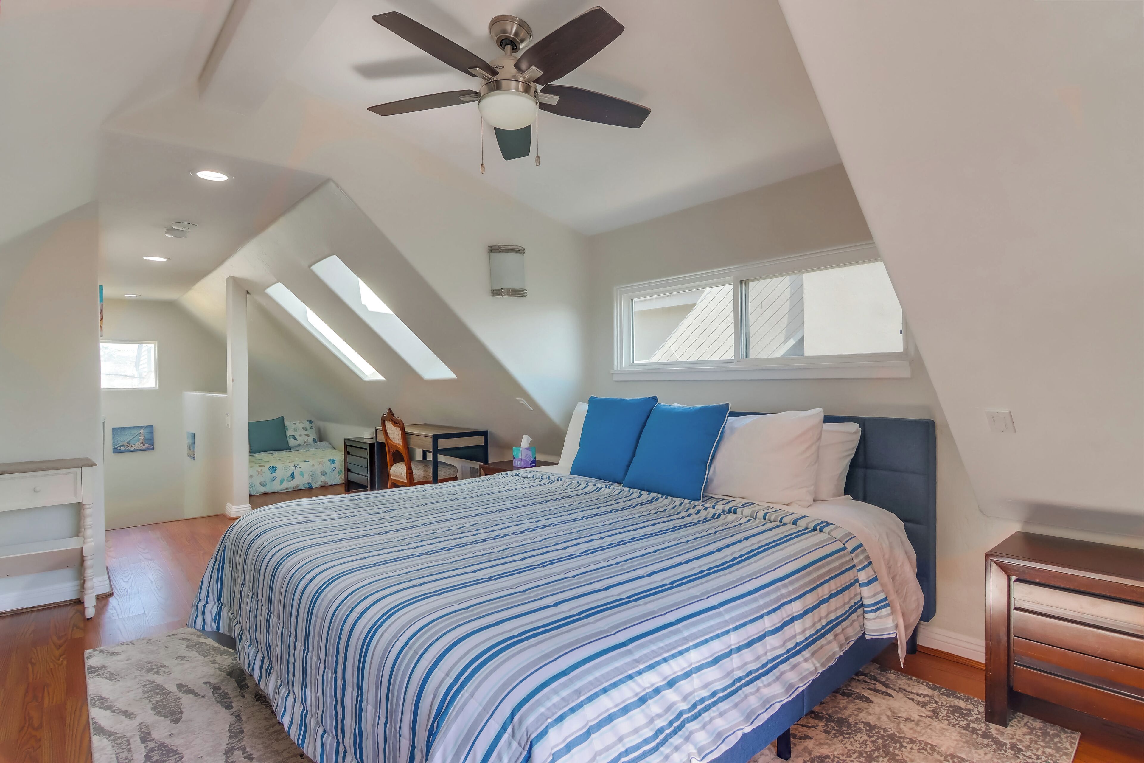 A bedroom with a bed, a ceiling fan, a window, and a skylight.