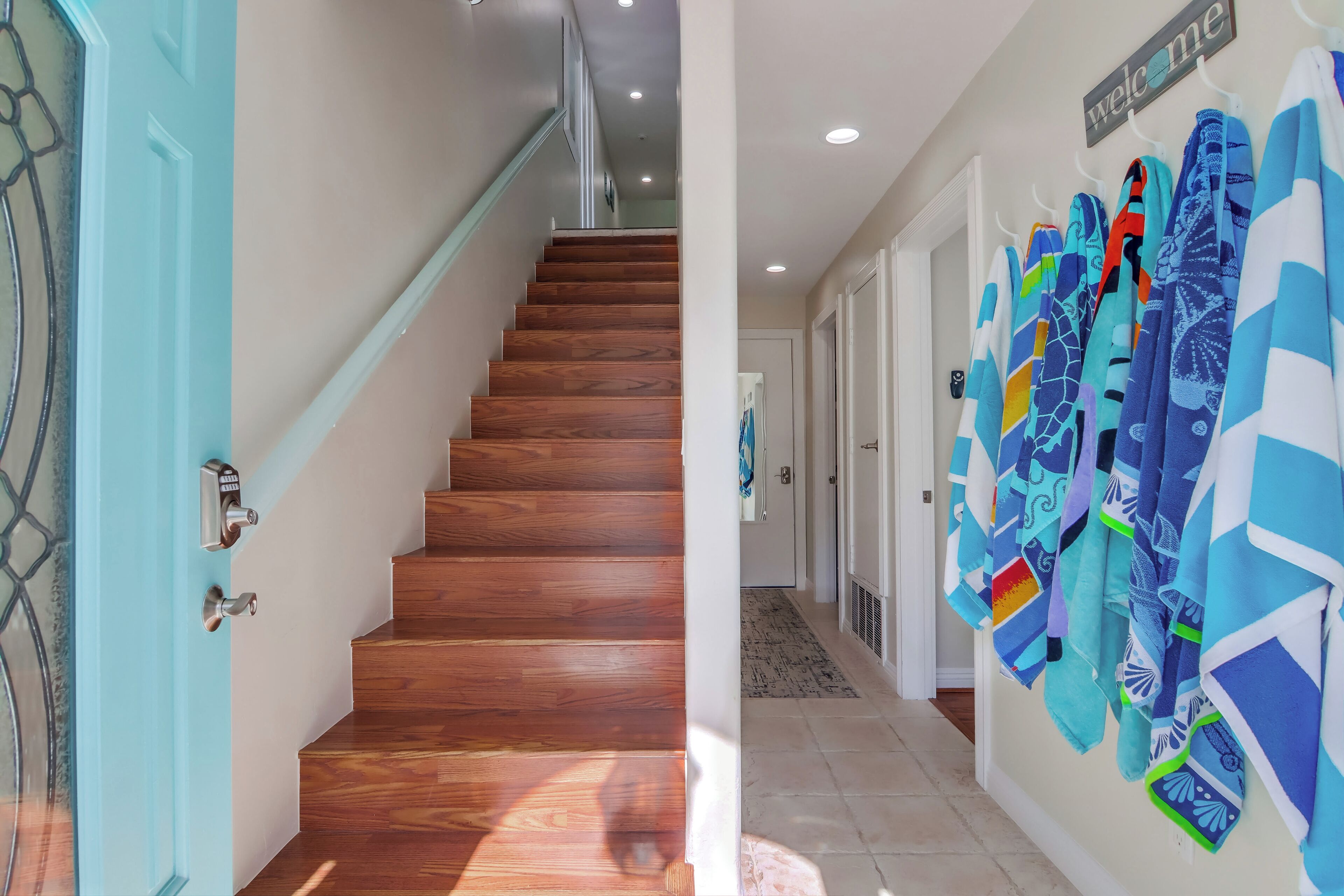 A staircase leading to a landing with a 'welcome' sign, a hallway with patterned tiles, and a wall with hanging towels.