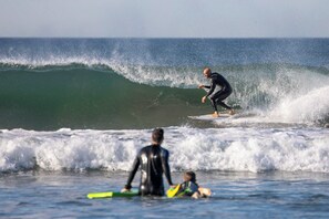 Eine Strandansicht mit Wellen, einem Surfer und einem Kind mit einem Surfbrett.