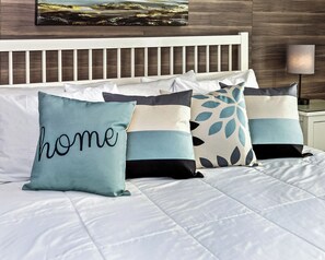 A bed with a white headboard and multiple pillows with text and leaf patterns.