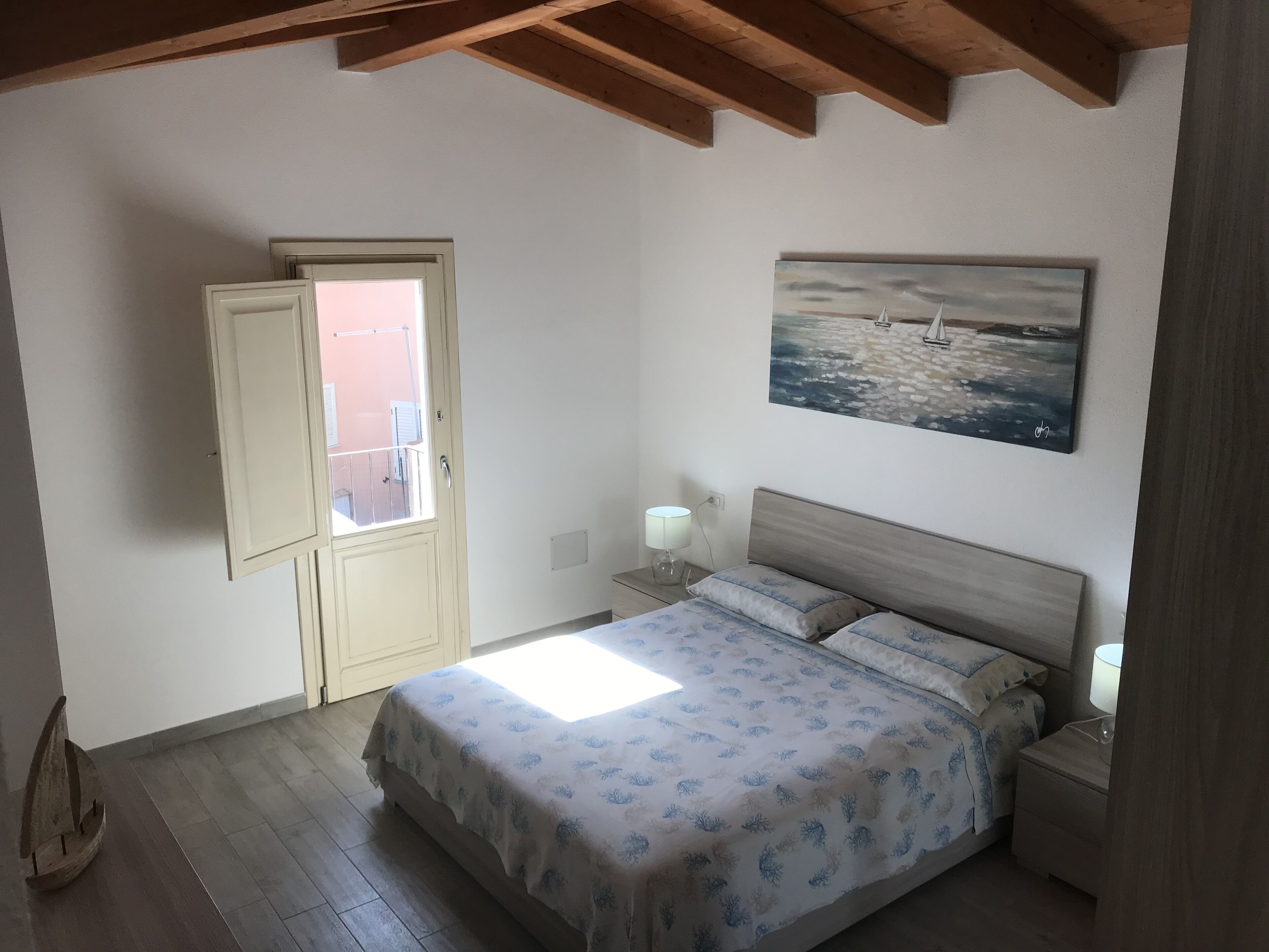 A bedroom with a bed, bedside lamps, a painting, a door, and a small wooden boat.