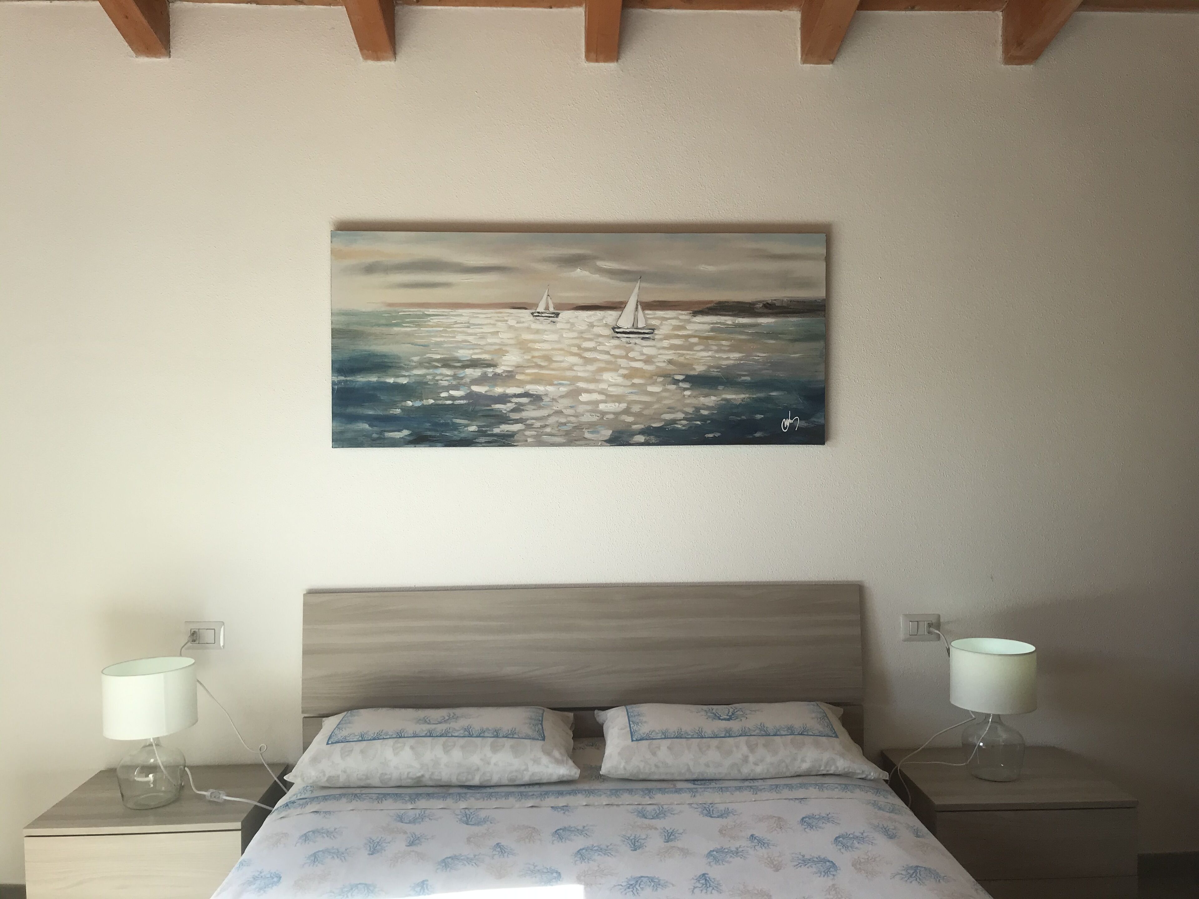 Een slaapkamer met een bed, twee bedlampjes, een nachtkastje en een schilderij van een zeilboot aan de muur.