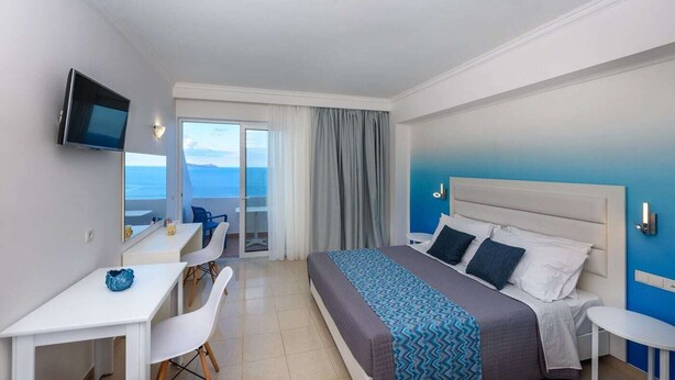Habitación de hotel con cama, escritorio, silla, televisión y vista al mar.