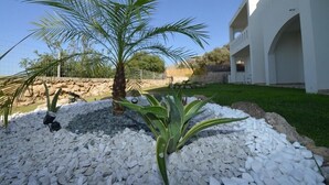 Un jardín ajardinado con una palmera, guijarros blancos y un edificio de arcos blancos.