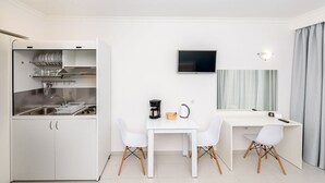 Habitación de hotel compacta con kitchenette, una zona de comedor con dos sillas, un televisor de pantalla plana y un espejo grande.