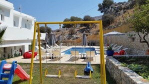 Un área de piscina con un conjunto de columpios, sillas de descanso y sombrillas.
