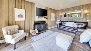 Una sala de estar con chimenea, un sofá, un sillón y un televisor.