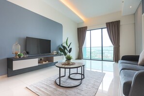 A modern living room with a flat-screen TV, a round coffee table, a sofa, and a large window with curtains.