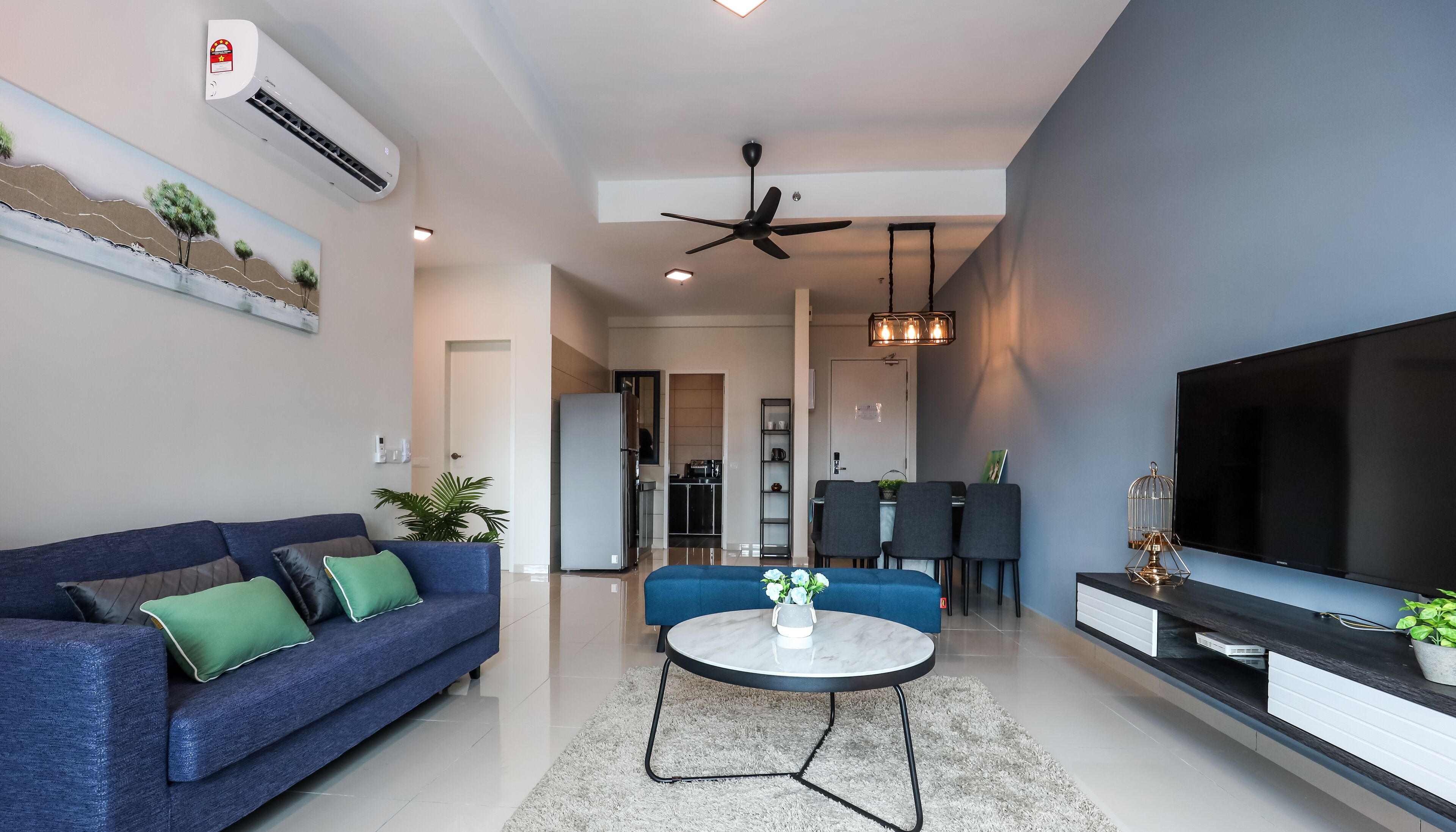 A modern living room with a blue sofa, a round coffee table, a TV, and a ceiling fan.