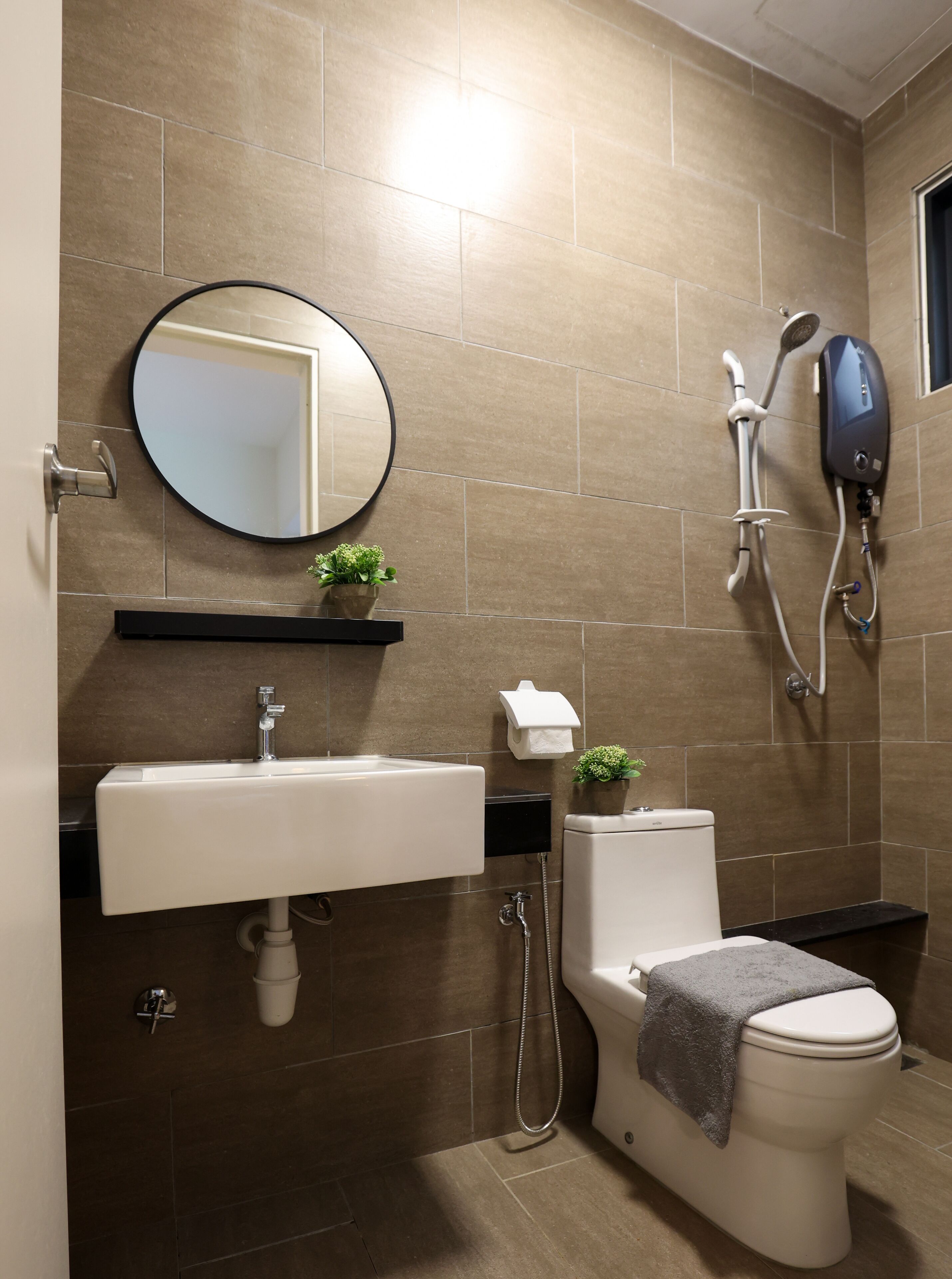 A modern bathroom with a white sink, a round mirror, a toilet, and a shower unit.