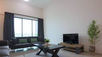 Una sala de estar moderna con un sofá, una mesa de centro, un televisor sobre un mueble bajo y una planta en maceta.