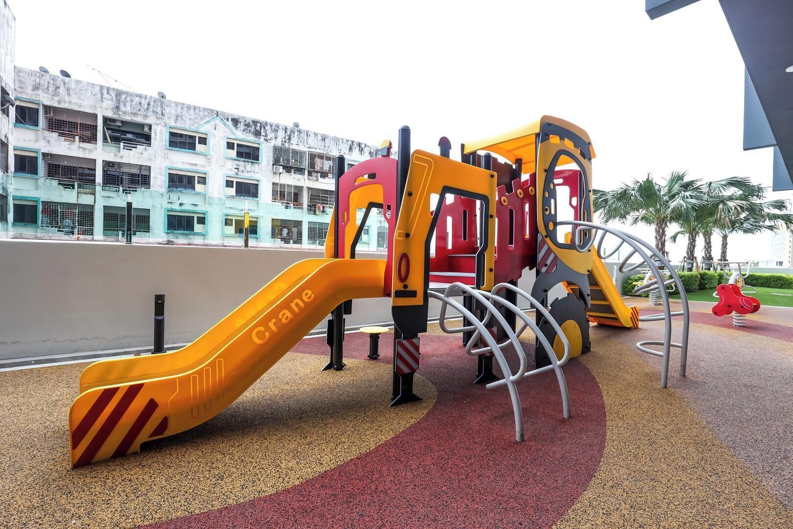A playground with a slide and climbing structures, surrounded by a building with multiple floors and balconies.