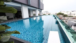 Une piscine intérieure moderne, avec une eau d’un bleu cristallin, entourée d’une rambarde en verre et offrant une vue sur le paysage urbain.