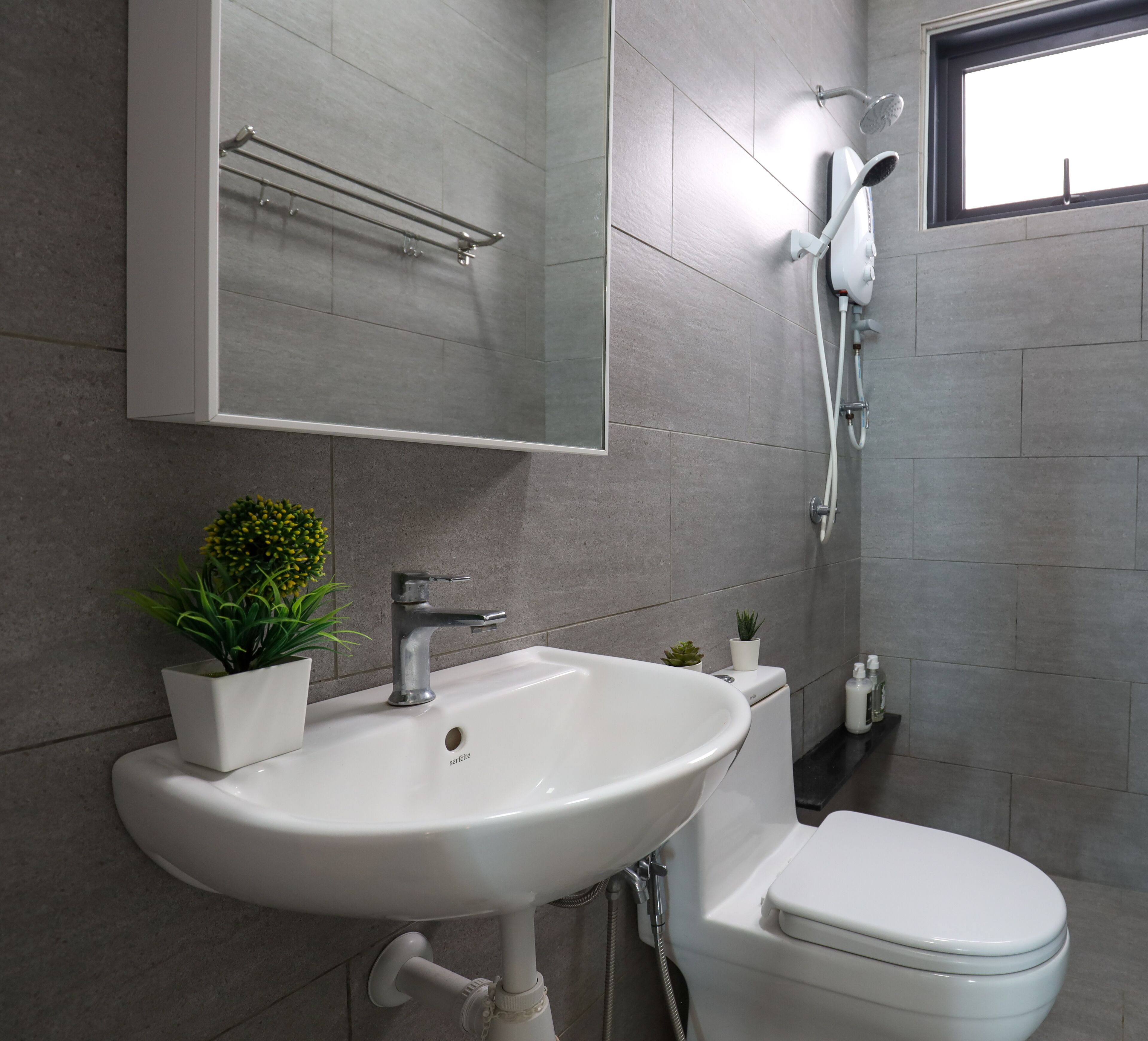Ein modernes Badezimmer mit Waschbecken, Spiegel und Toilette. Eine Duschbrause ist an der Wand montiert und auf dem Waschbecken steht ein kleiner Topfpflanze.