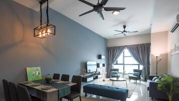 A modern living room with a dining area, two ceiling fans, a large window with curtains, and a flat-screen TV.