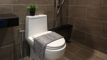 A modern bathroom with a shower, toilet, and a small potted plant.