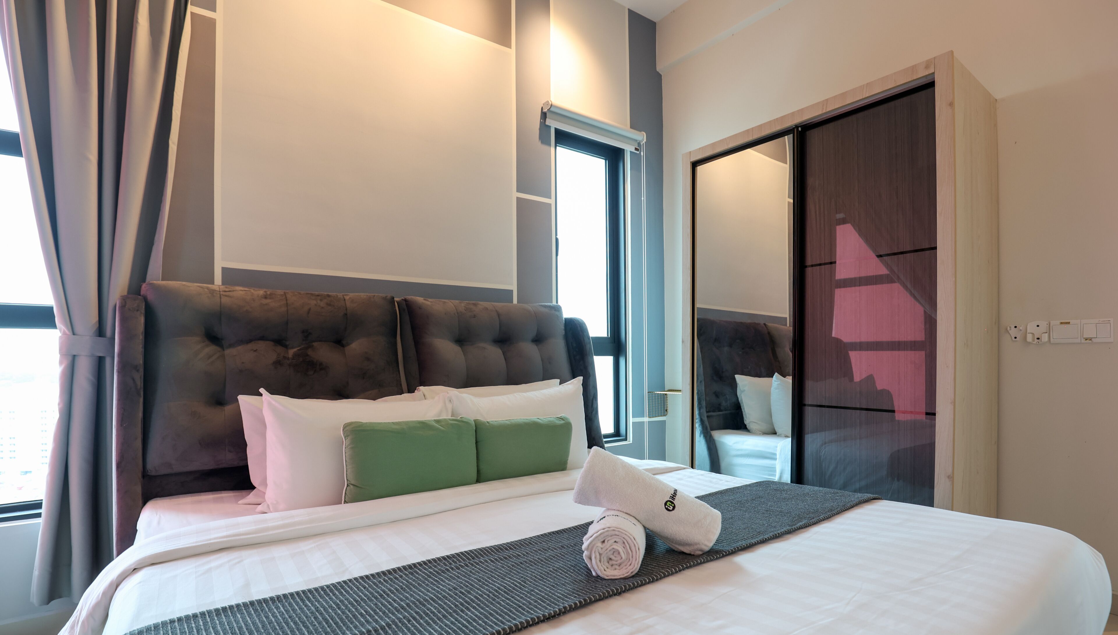 A hotel room with a large bed, a headboard, a window with curtains, and a mirror.