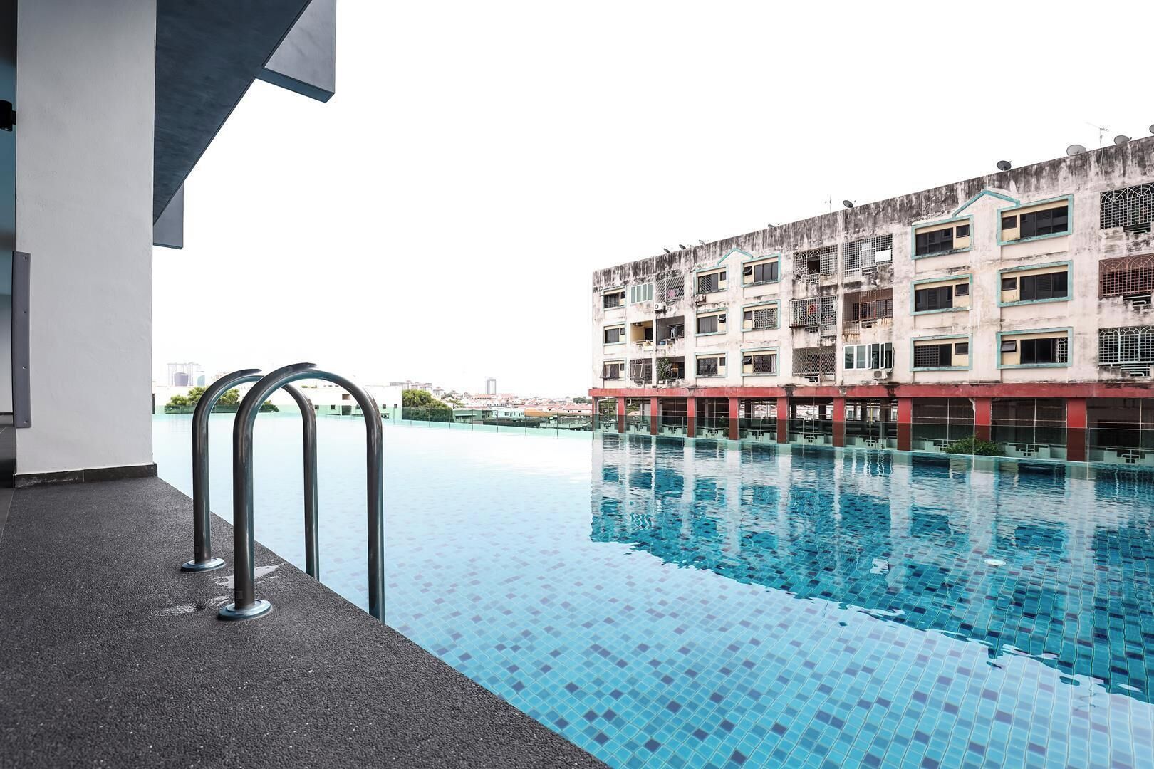 A swimming pool with a tiled floor, a metal handrail, and a building with multiple balconies in the background.