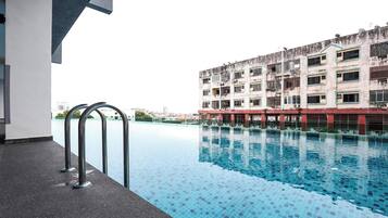 A swimming pool with a tiled floor, a metal handrail, and a building with multiple balconies in the background.