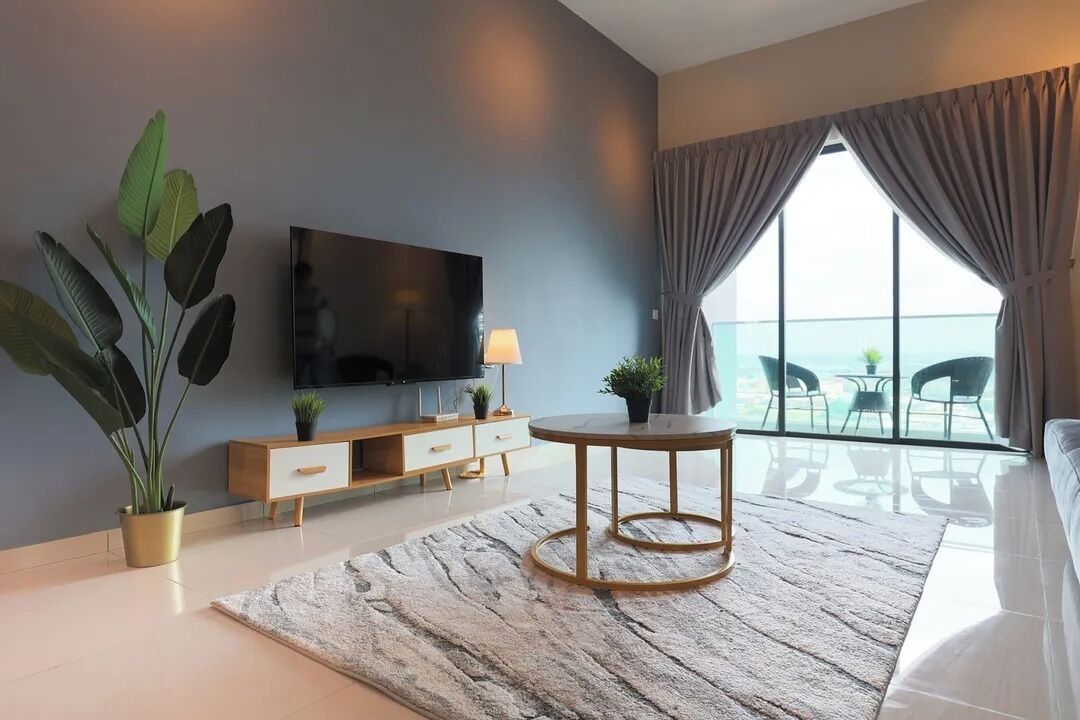 A modern hotel room with a large TV, a round table, a sofa, and a balcony with a view.