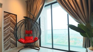 Una habitación moderna con un gran ventanal, un sillón colgante con cojines rojos y una planta en maceta.