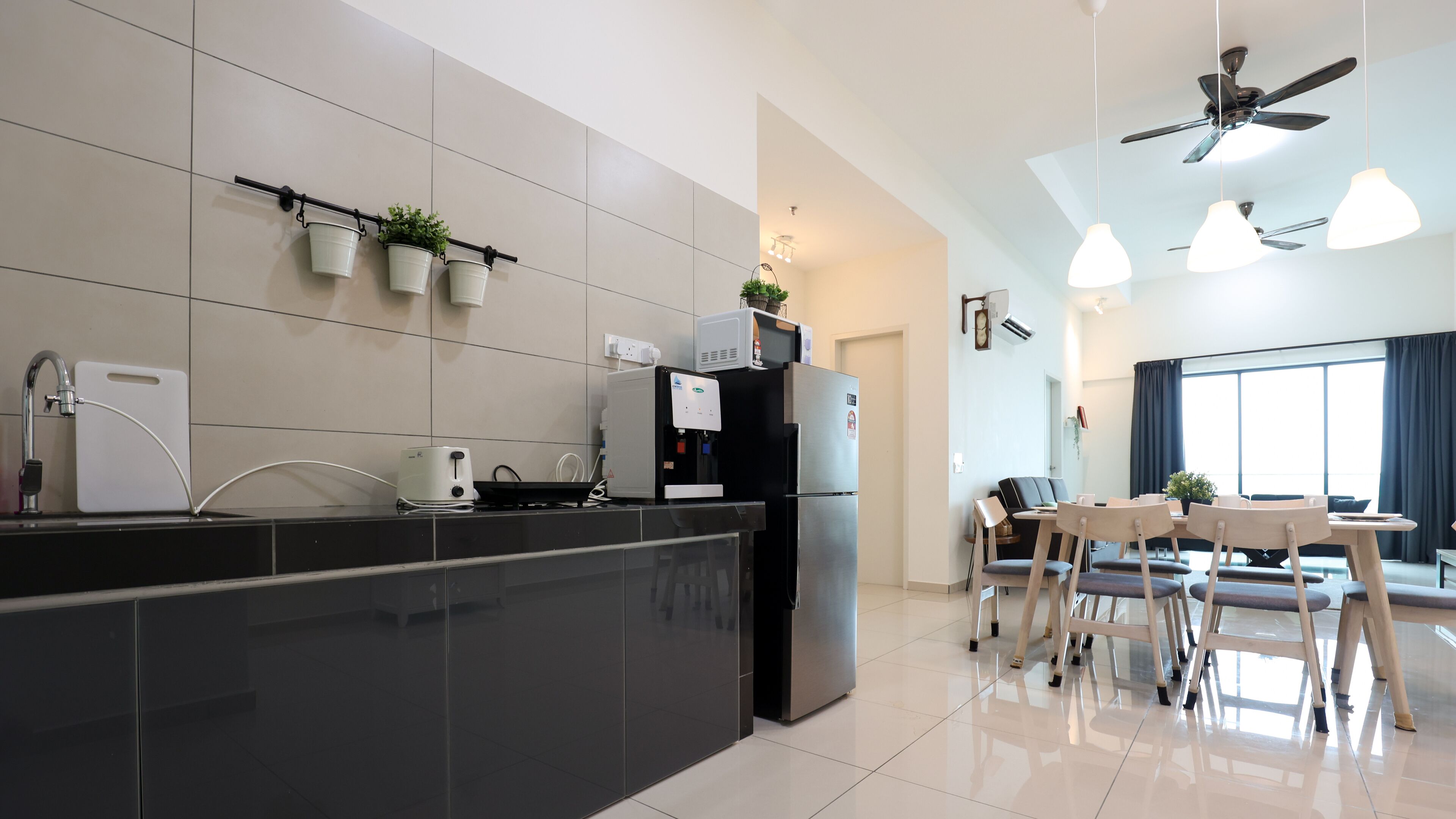 A modern kitchen with a black countertop, a built-in oven, and a refrigerator. There are potted plants on the wall and a dining area with a table and chairs.
