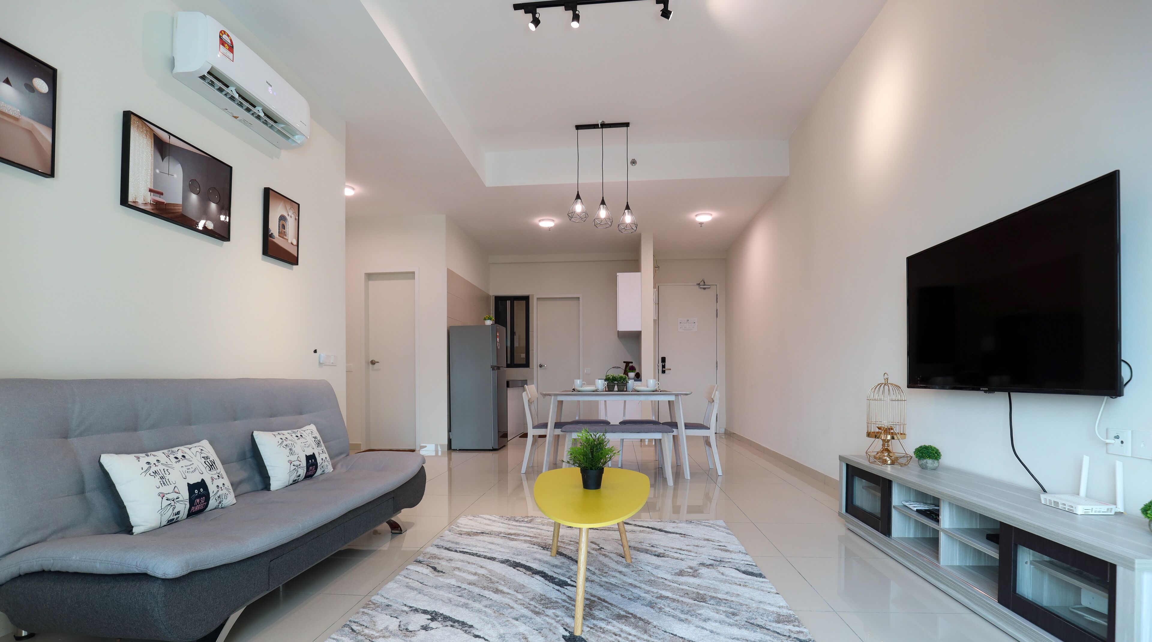 A modern living room with a grey sofa, a yellow coffee table, and a flat-screen TV mounted on the wall.